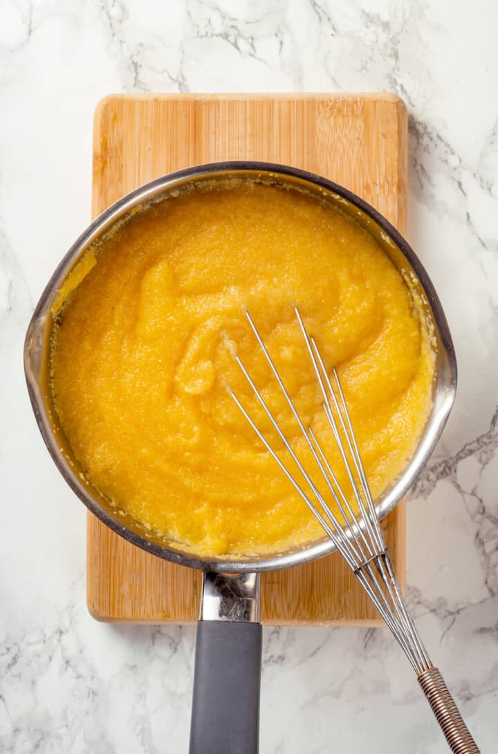 Overhead view of creamy polenta in saucepan with whisk