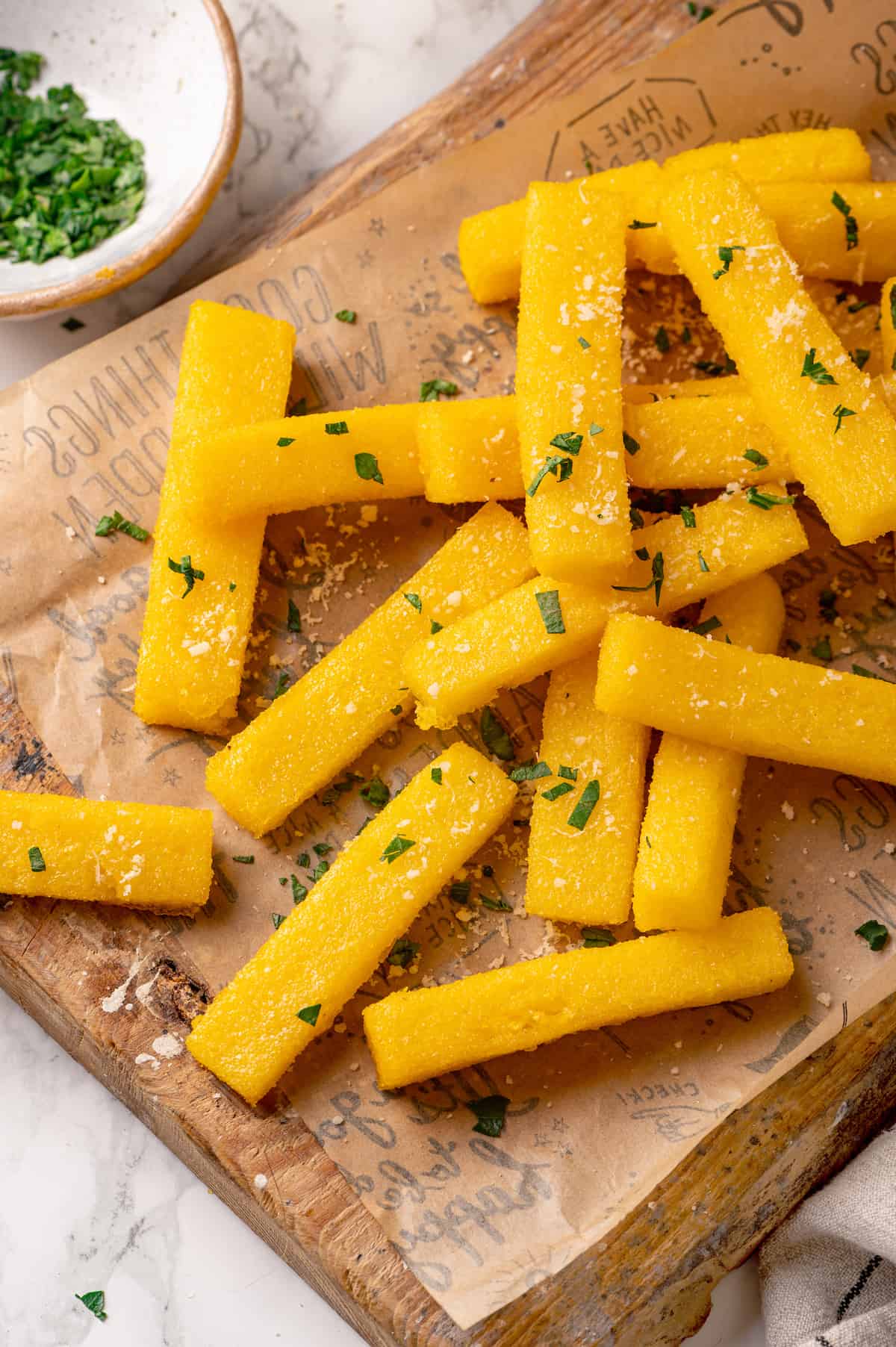Crispy polenta fries on parchment paper with bowl of parsley in background
