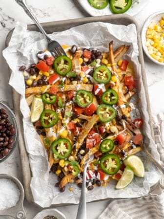 Overhead view of loaded nacho fries on sheet pan with forks