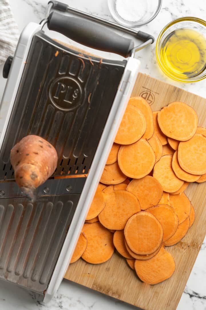 Overhead view of sweet potato being sliced on mandoline