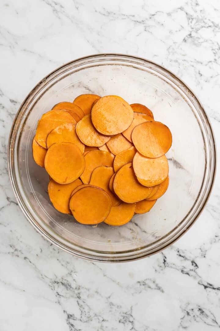 Overhead view of sweet potato slices in bowl with oil
