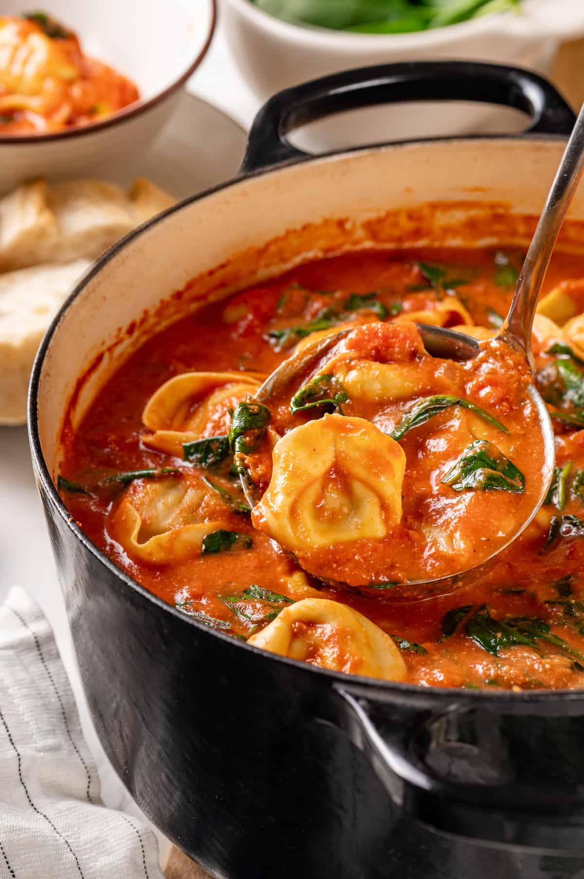 Spoon lifting tomato tortellini soup from pot