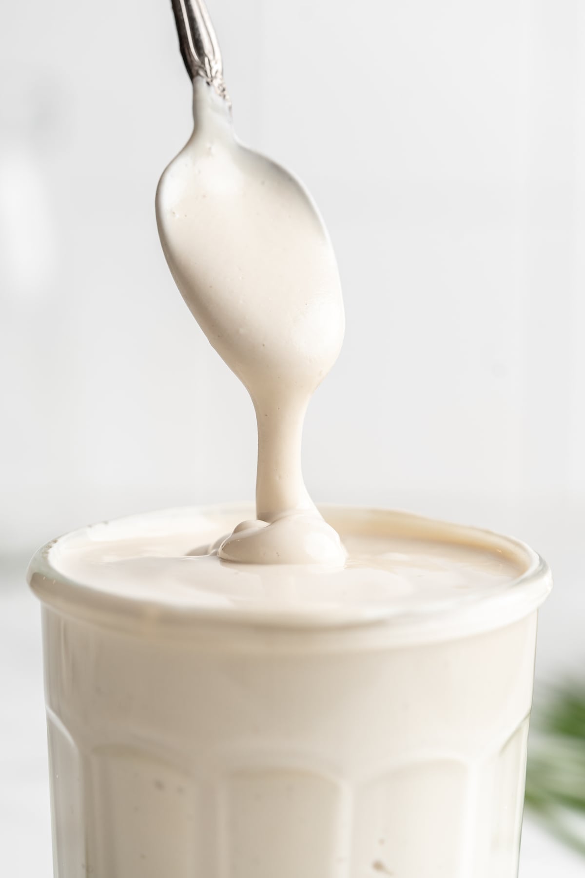 Spoon dripping vegan sour cream into jar