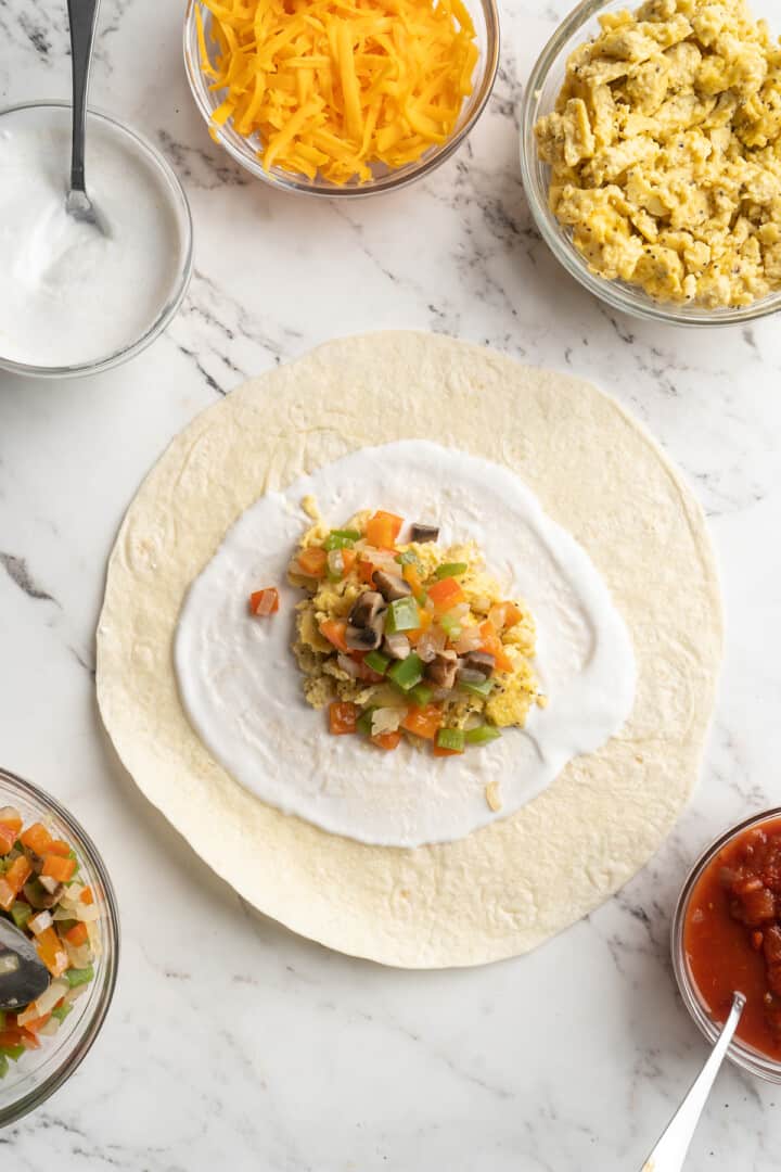 Overhead view of tortilla topped with vegan yogurt, vegan scramble, and veggies