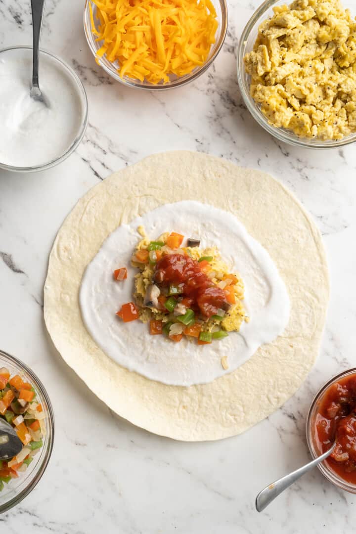 Overhead view of tortilla topped with vegan yogurt, vegan scramble, veggies, and salsa