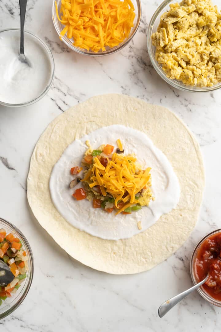 Overhead view of tortilla topped with vegan yogurt, vegan scramble, veggies, and cheese
