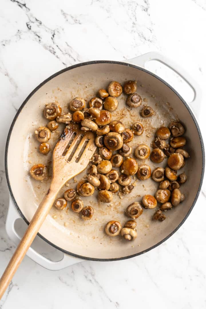 Overhead view of mushrooms browning in skillet with garlic