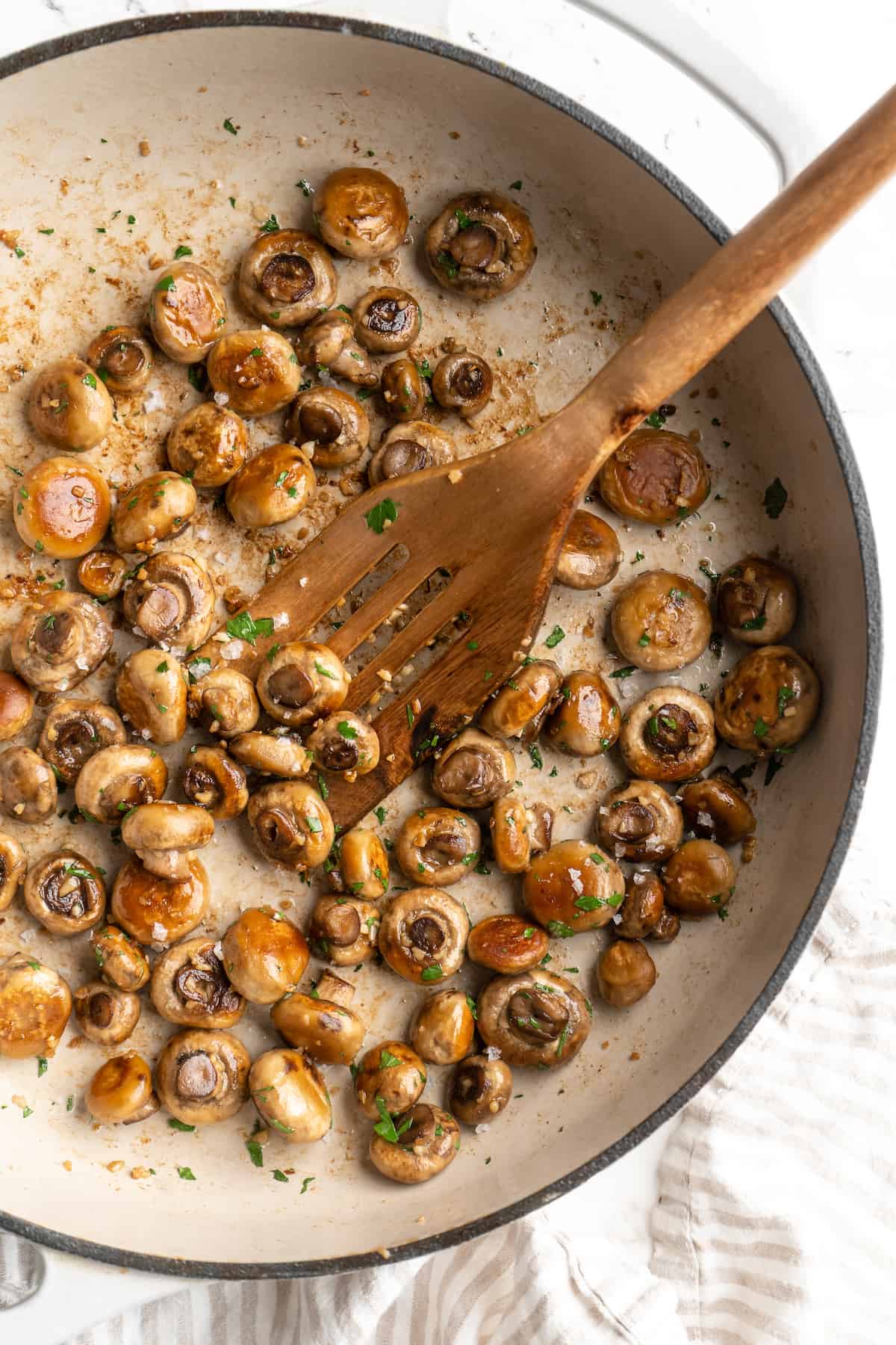 Overhead view of garlic mushrooms in skillet with spatula