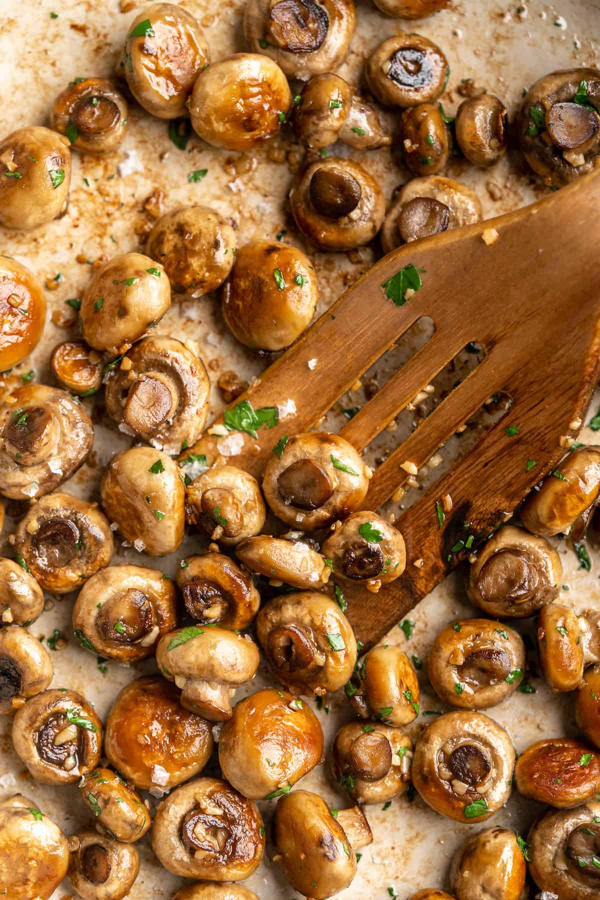Garlic mushrooms in skillet with wooden spatula