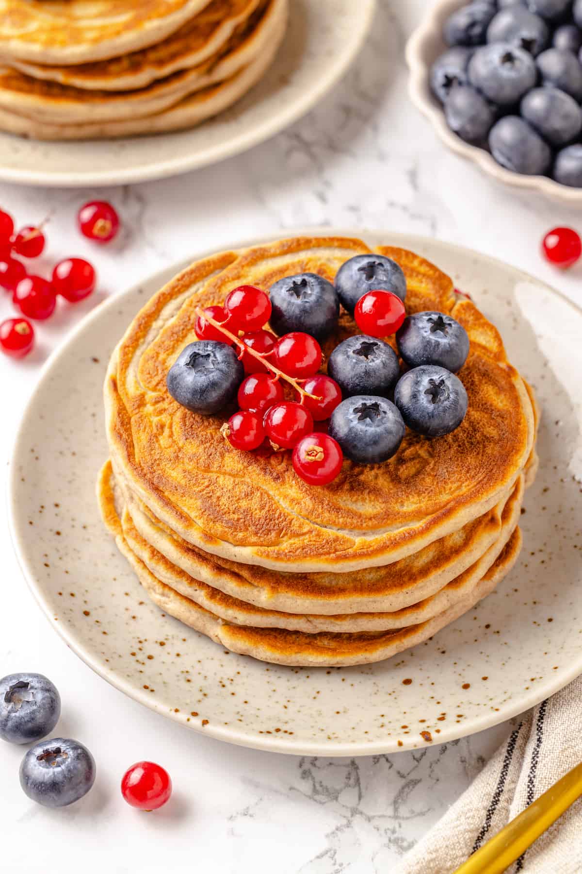 Stack of protein pancakes on plate with fresh berries on top
