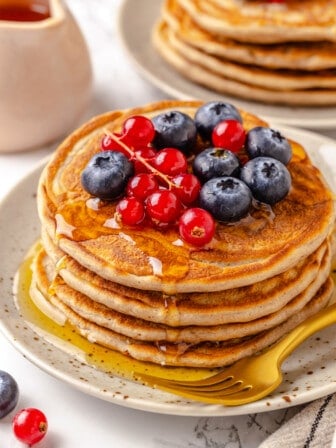 Stack of 4 protein pancakes on plate with maple syrup and berries