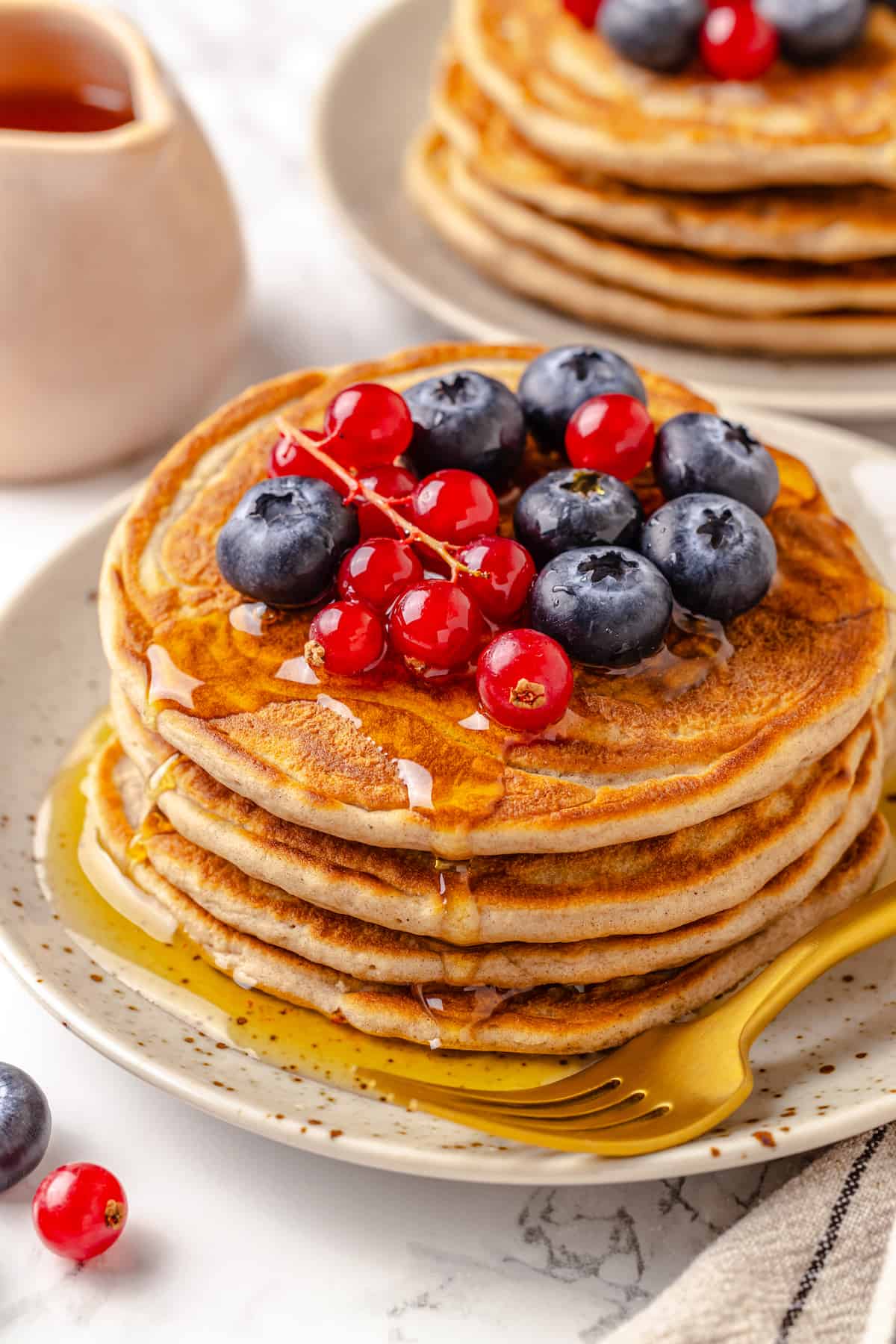 Stack of 4 protein pancakes on plate with maple syrup and berries