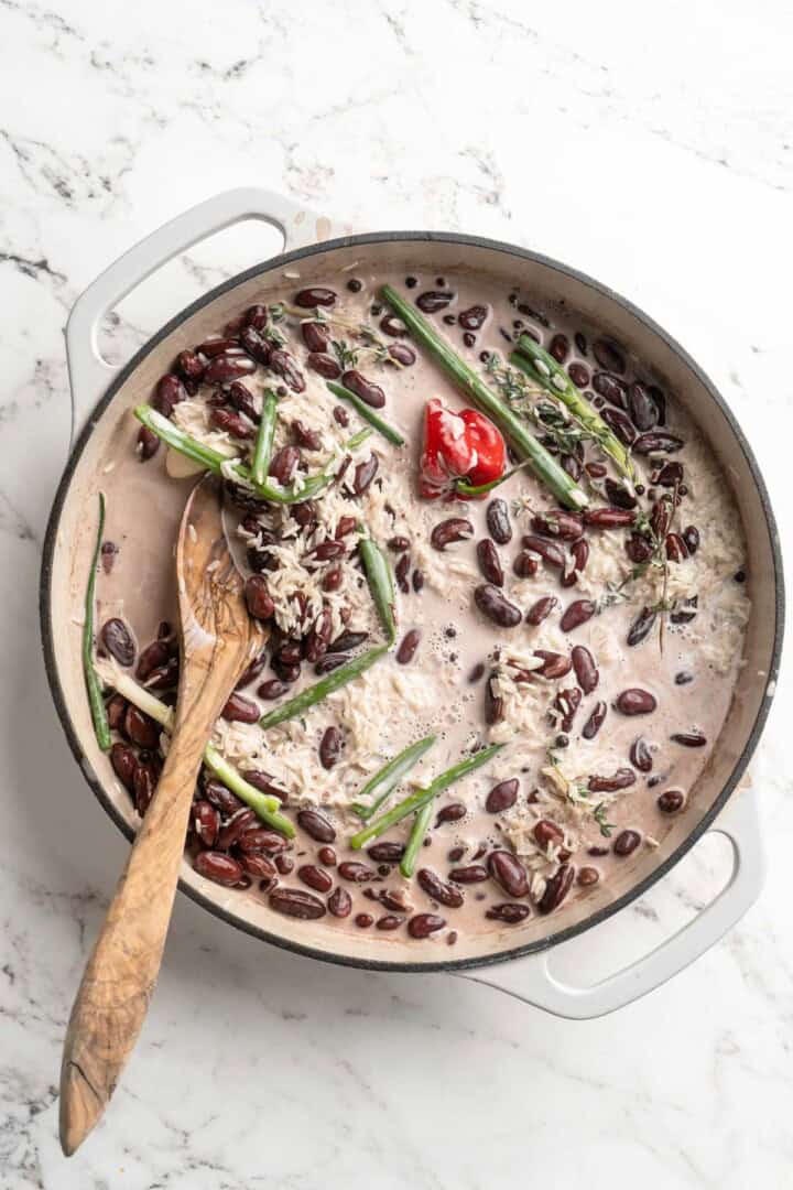 Coconut milk, rice, and aromatics added to pan of cooked kidney beans