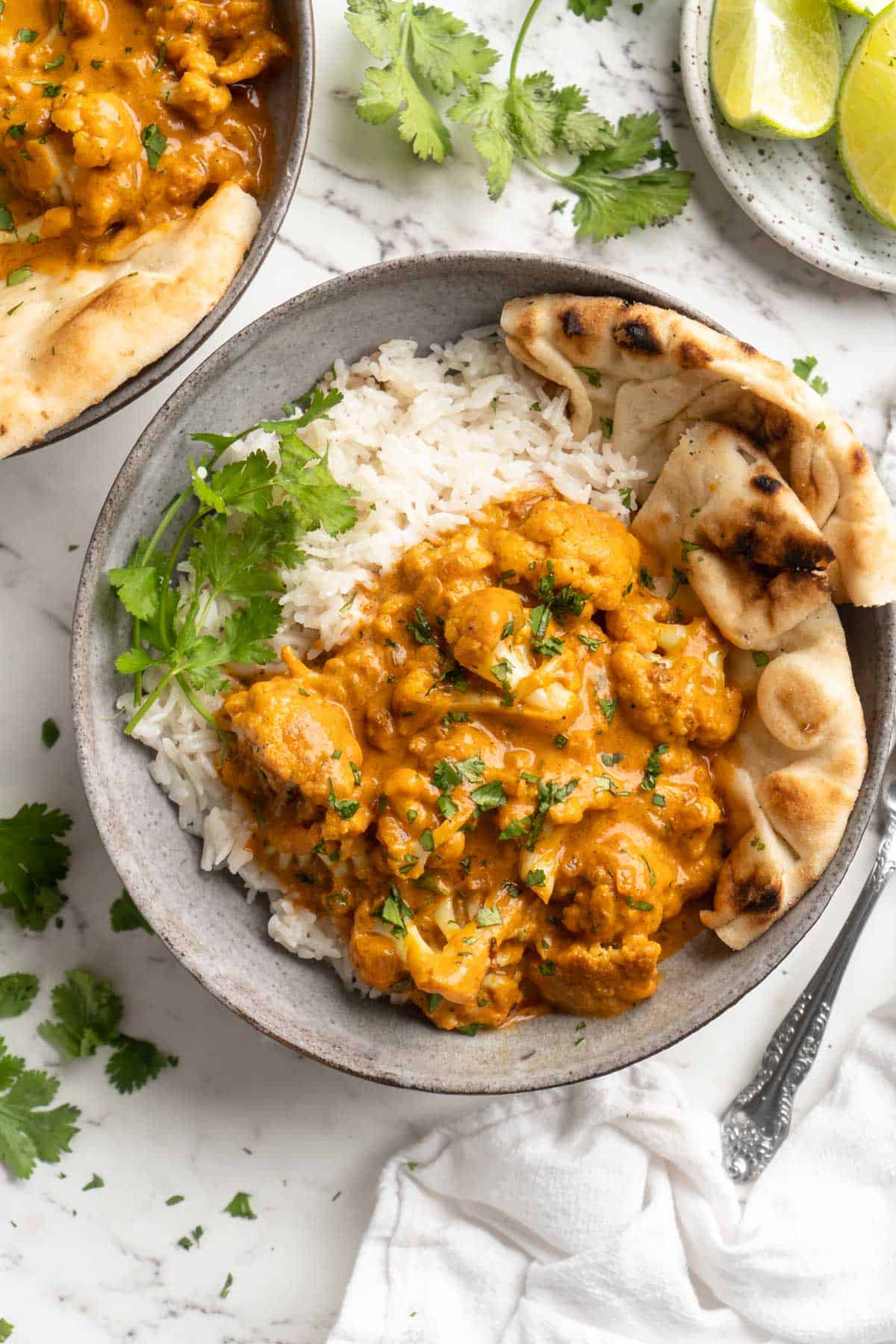 Overhead view of butter cauliflower in bowl with rice and naan