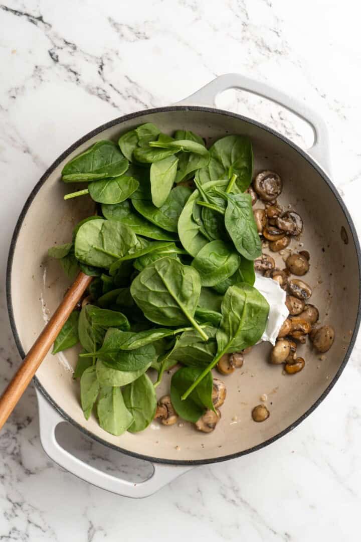 Overhead view of spinach added to skillet of mushrooms