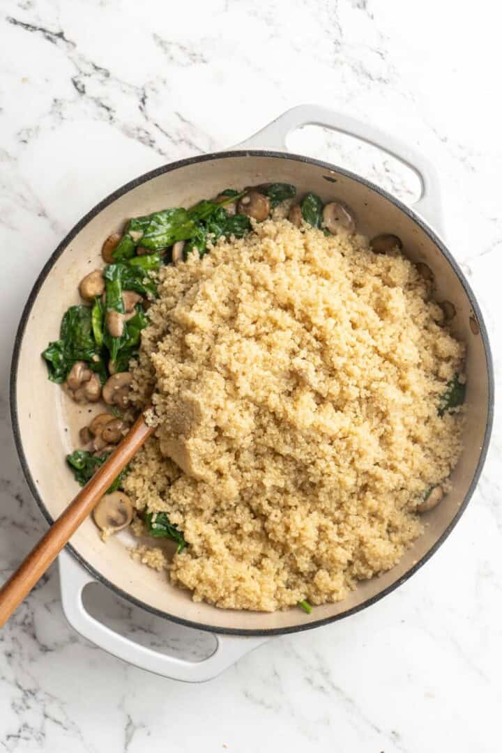 Overhead view of quinoa added to pan of sauteed spinach and mushrooms