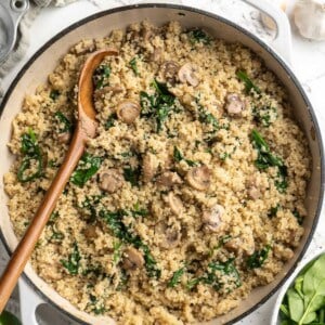 Overhead view of coconut creamy spinach and mushroom quinoa in skillet with wooden spoon