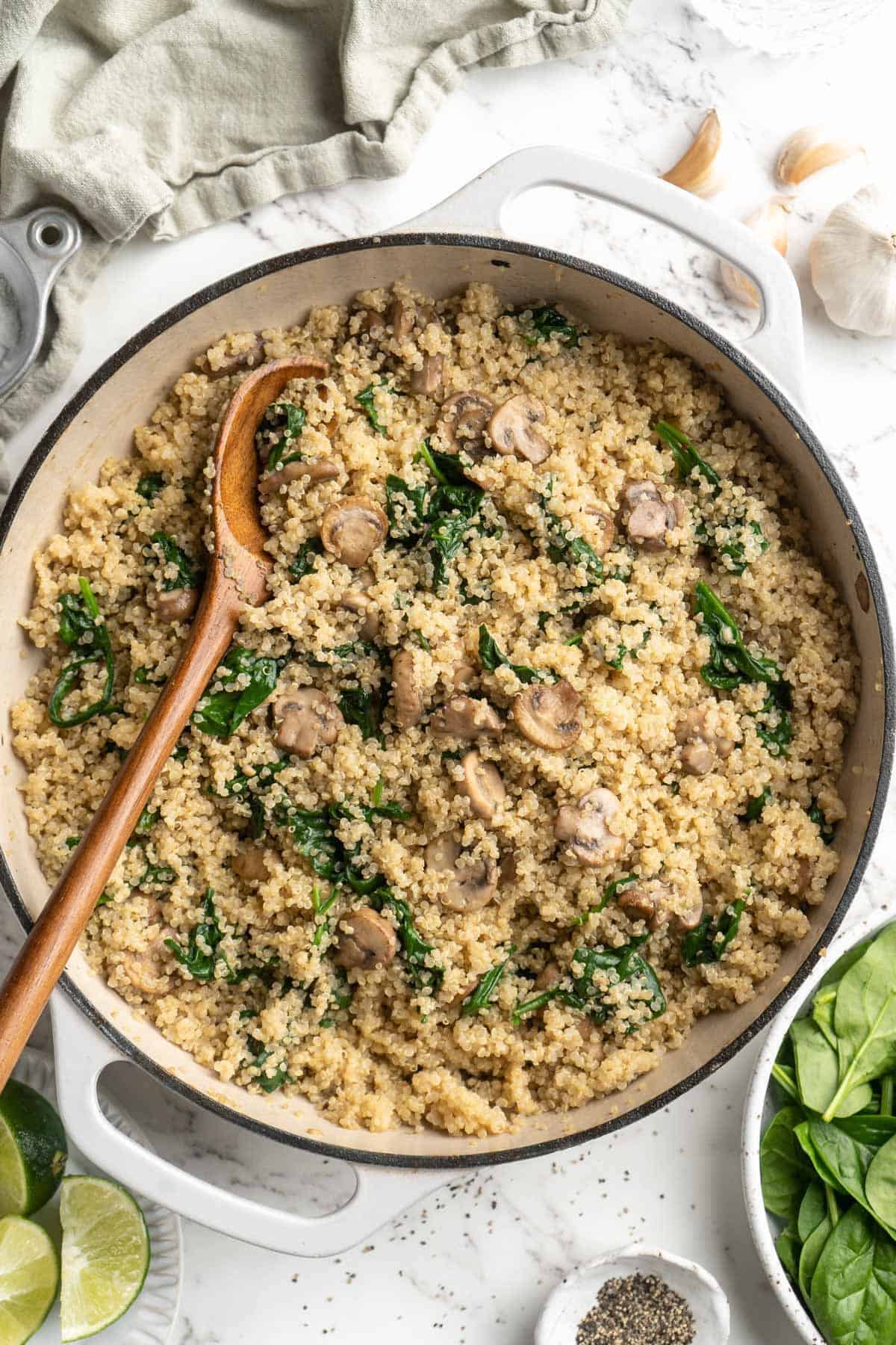 Overhead view of coconut creamy spinach and mushroom quinoa in skillet with wooden spoon