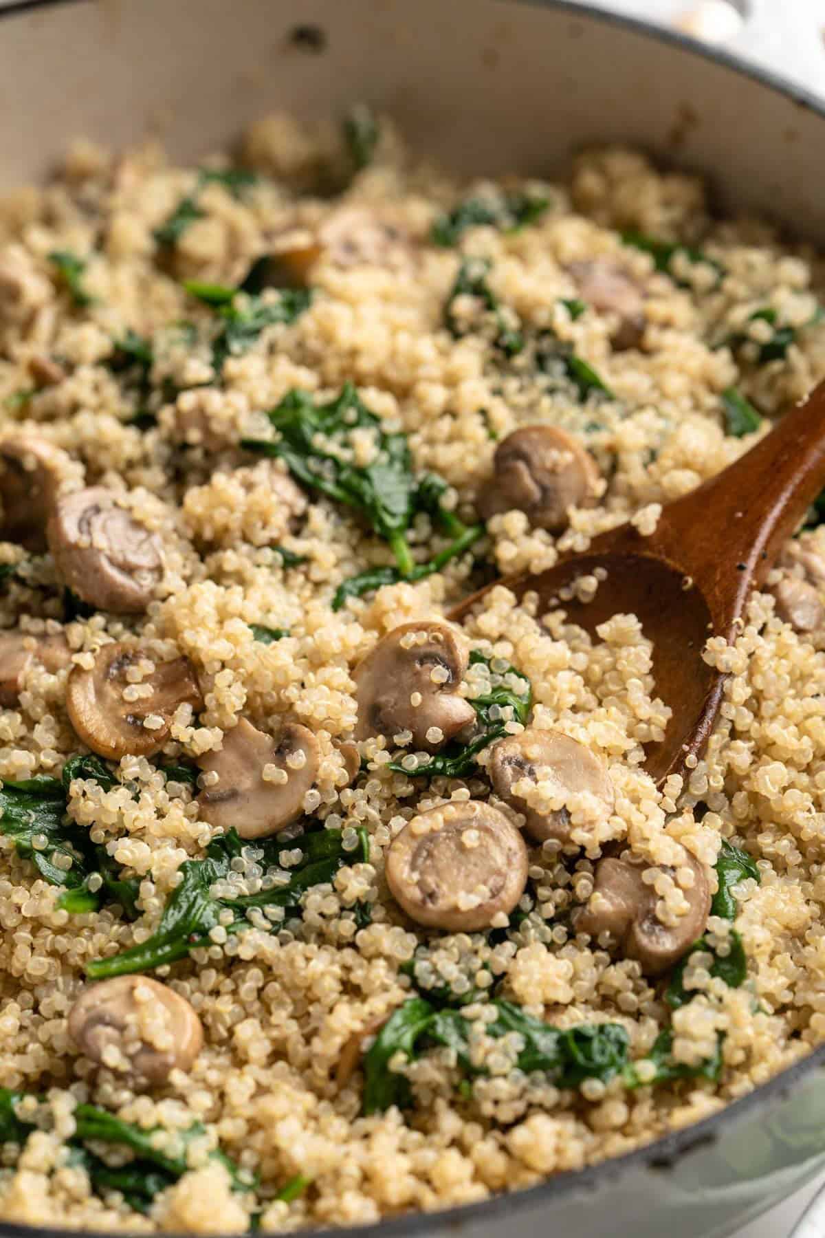 Skillet of coconut creamy spinach and mushroom quinoa with wooden spoon