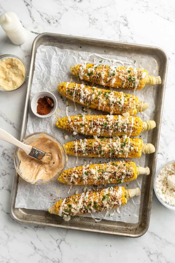 Overhead view of Mexican street corn on sheet pan with bowl of mayo mixture