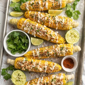 Overhead view of elotes on sheet pan with toppings and garnishes