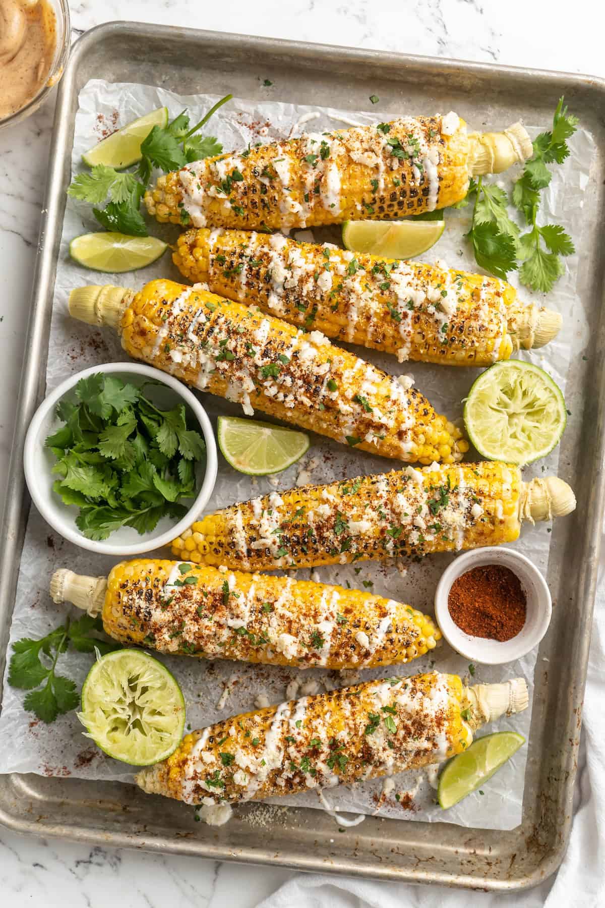 Overhead view of elotes on sheet pan with toppings and garnishes