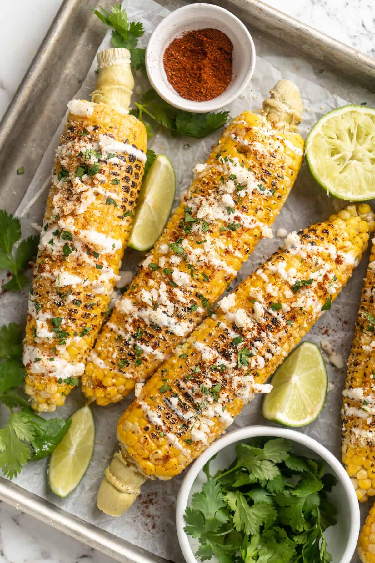 Overhead view of Mexican street corn on a sheet pan with toppings