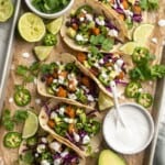 Overhead view of sweet potato and black bean tacos on parchment-lined baking sheet with toppings