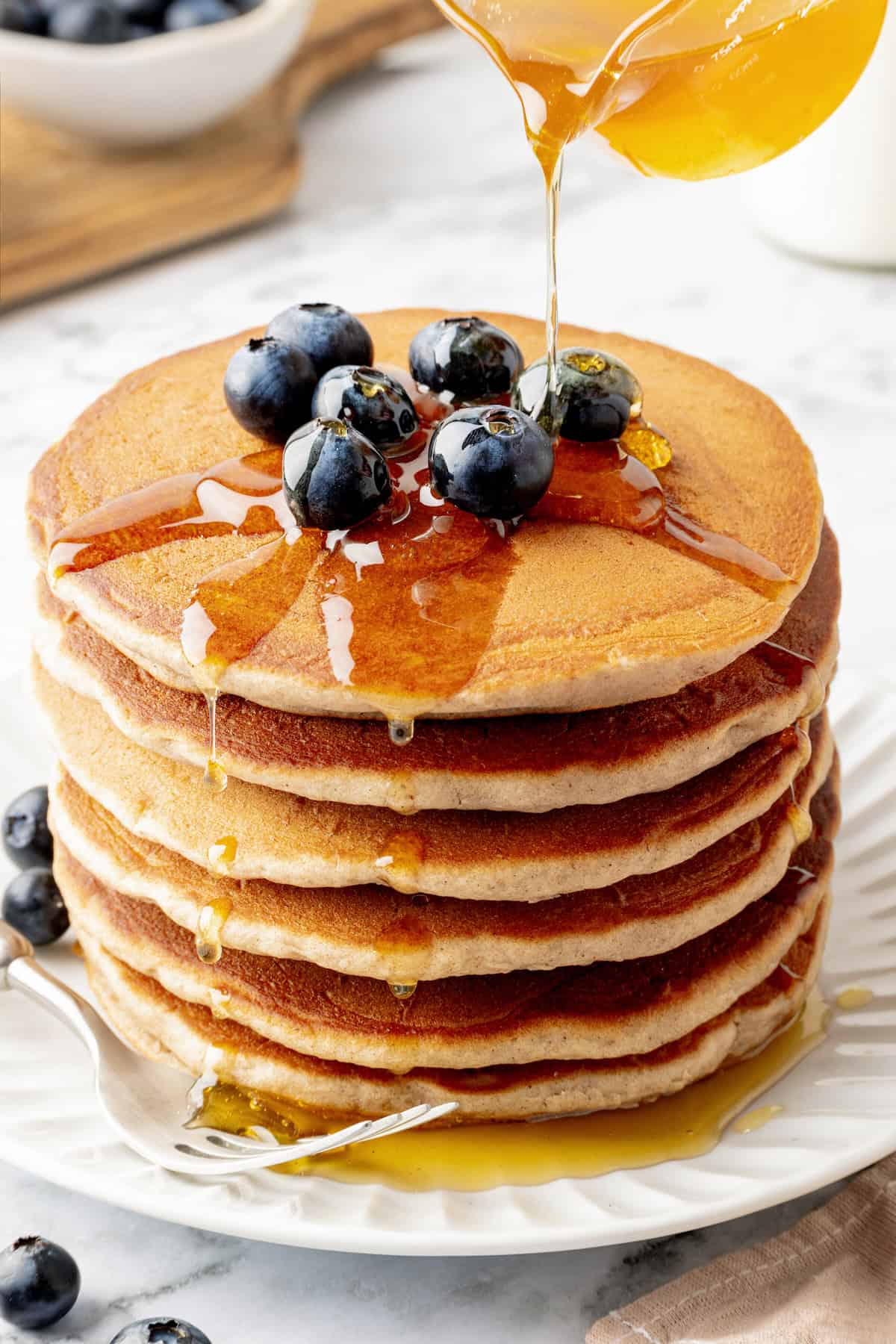 Pouring maple syrup onto stack of buckwheat pancakes