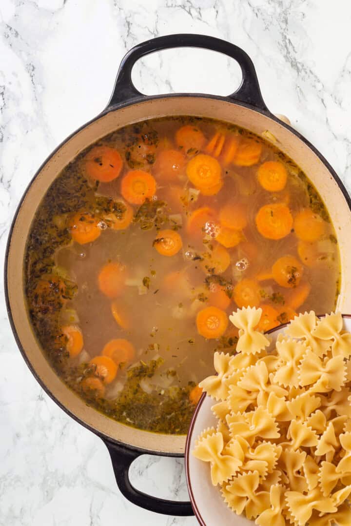 Adding bowtie pasta to pot of vegan chicken noodle soup