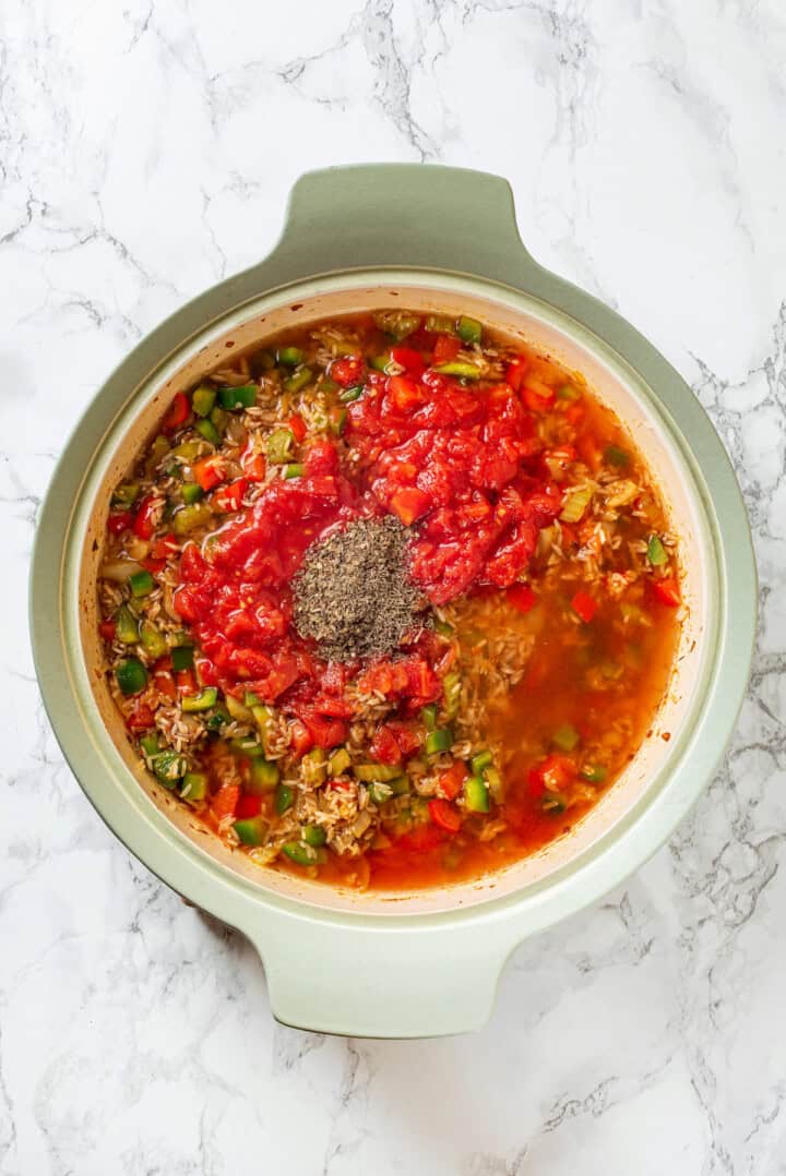 Overhead view of broth, herbs, and diced tomatoes added to vegan jambalaya