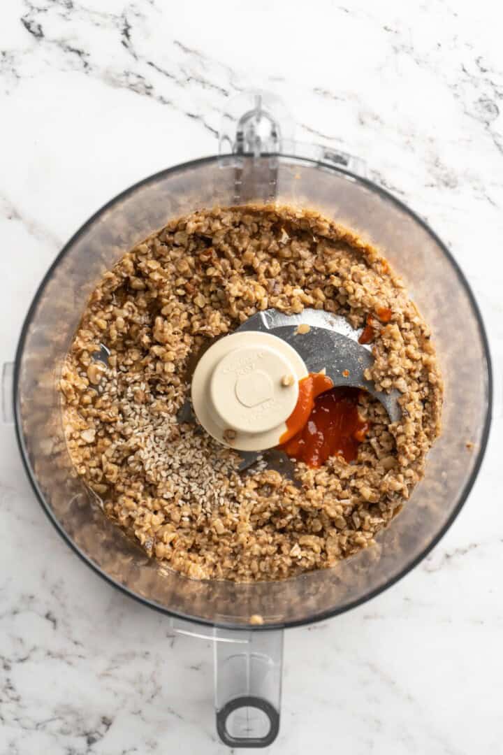 Overhead view of sauce ingredients added to walnut meat in food processor