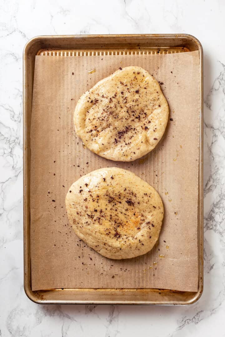 Seasoned and oiled pitas on baking sheet