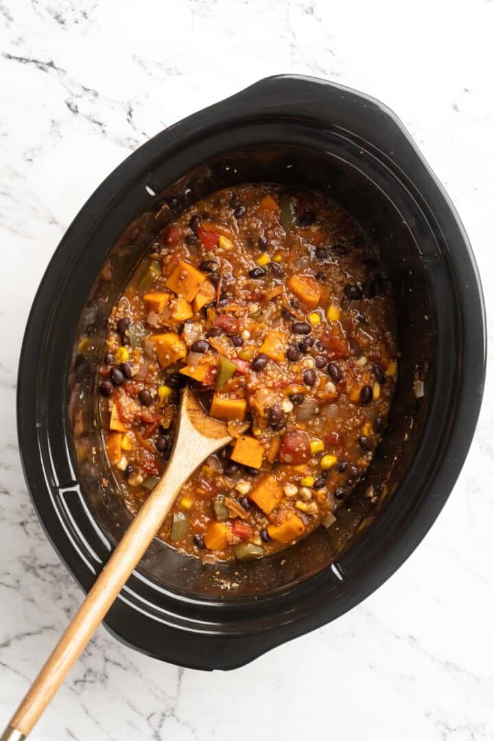 Overhead view of vegan sweet potato and black bean chili in slow cooker insert with wooden spoon