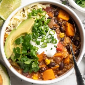 Overhead view of sweet potato and black bean chili in bowl with cashew sour cream, avocado, cilantro, and green onion