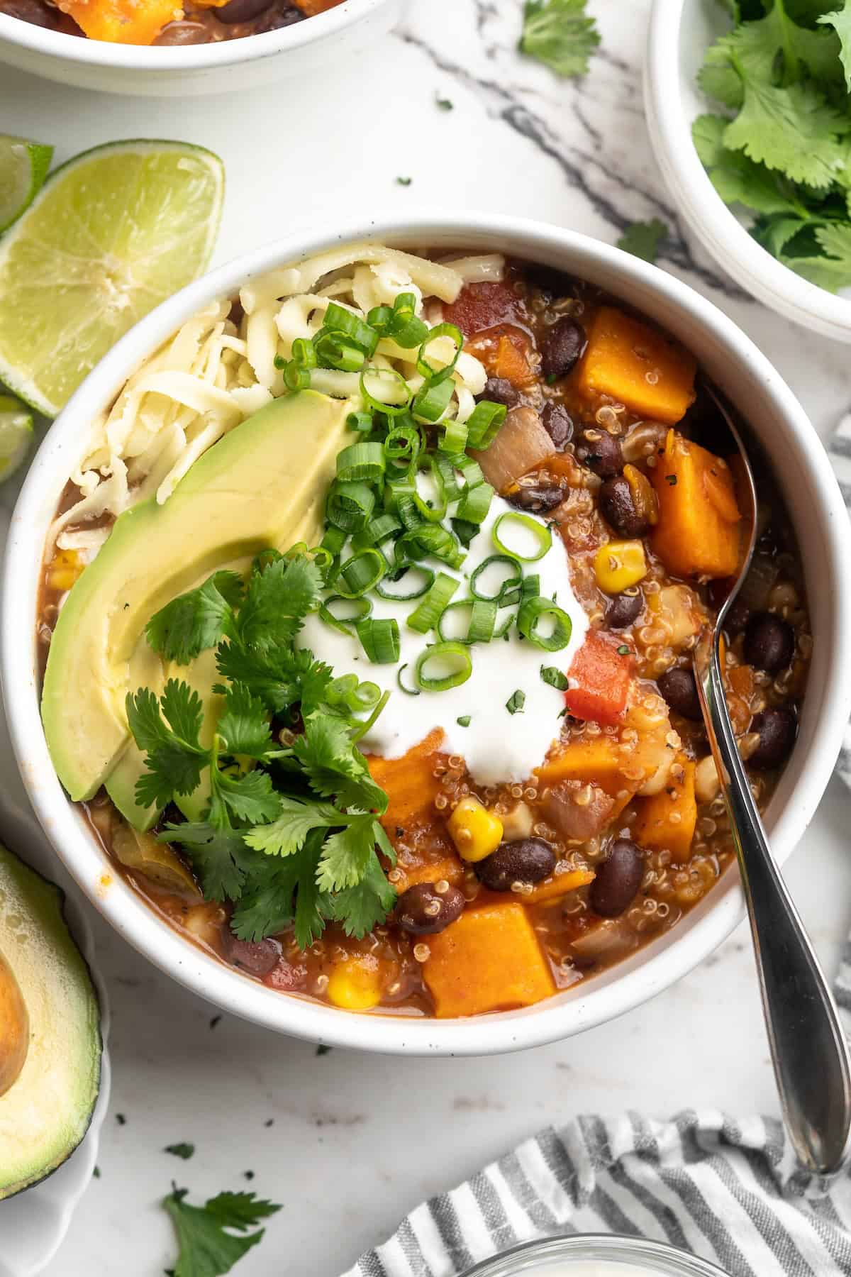 Overhead view of sweet potato and black bean chili in bowl with cashew sour cream, avocado, cilantro, and green onion