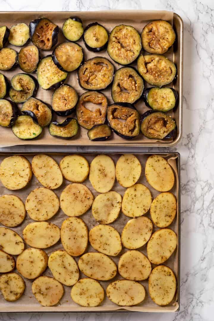 Overhead view of seasoned eggplant and potato slices on pans