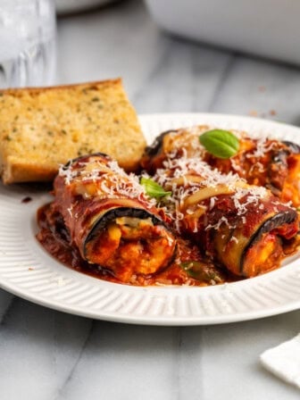 Side view of vegan eggplant rollatini on plate with garlic bread