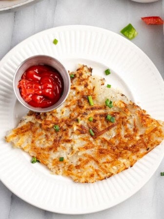 Overhead view of crispy hash browns on plate with ketchup