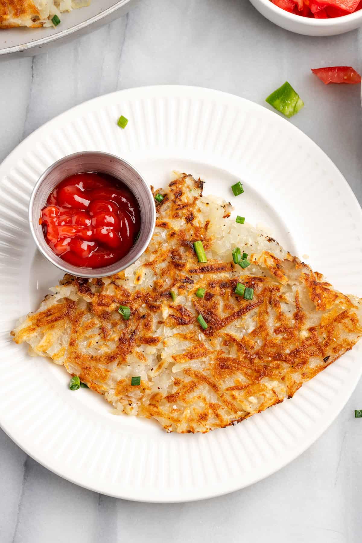 Overhead view of crispy hash browns on plate with ketchup