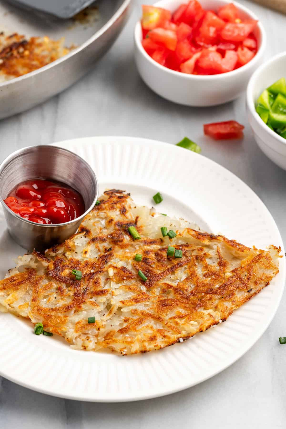 Crispy homemade hash browns on plate with cup of ketchup