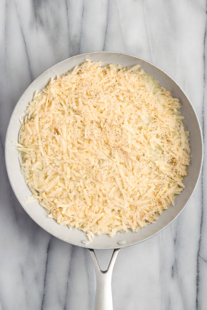 Overhead view of shredded potatoes in skillet