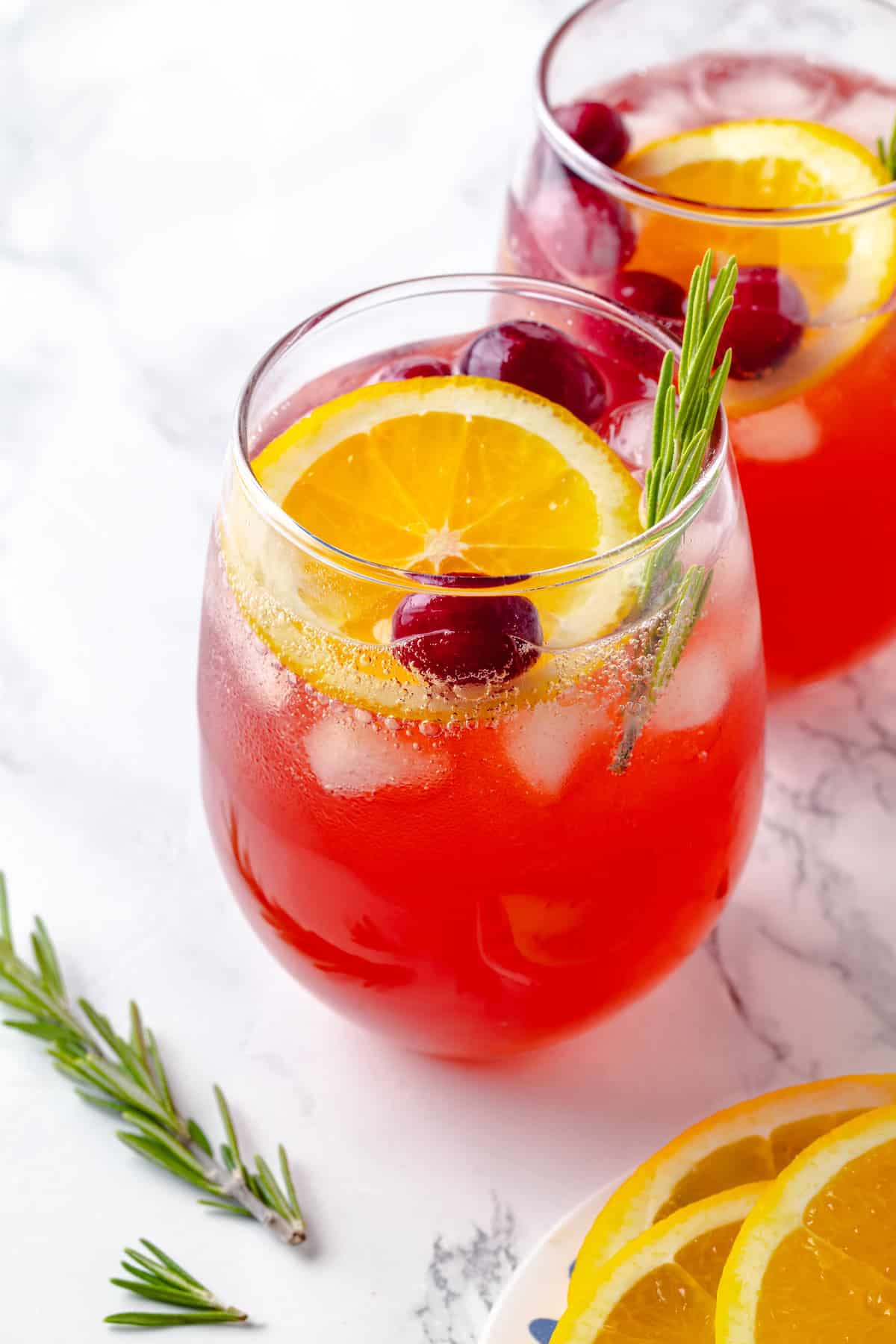 Two glasses of Christmas punch with orange slices, rosemary, and cranberries