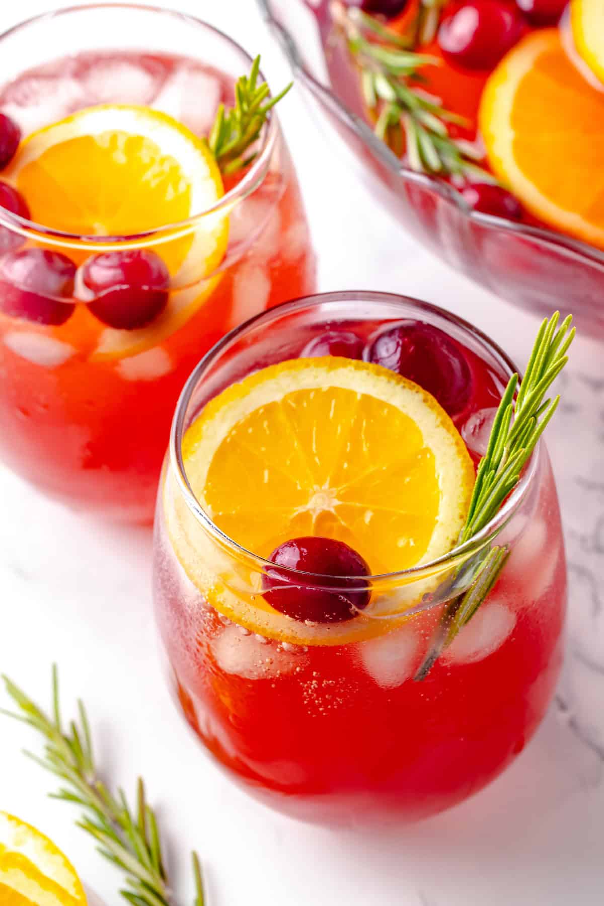 Two glasses of Christmas punch with orange slices, rosemary, and cranberries for garnish