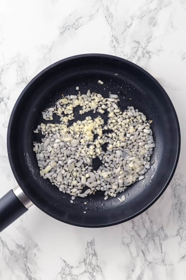 Overhead view of onions and garlic cooking in skillet