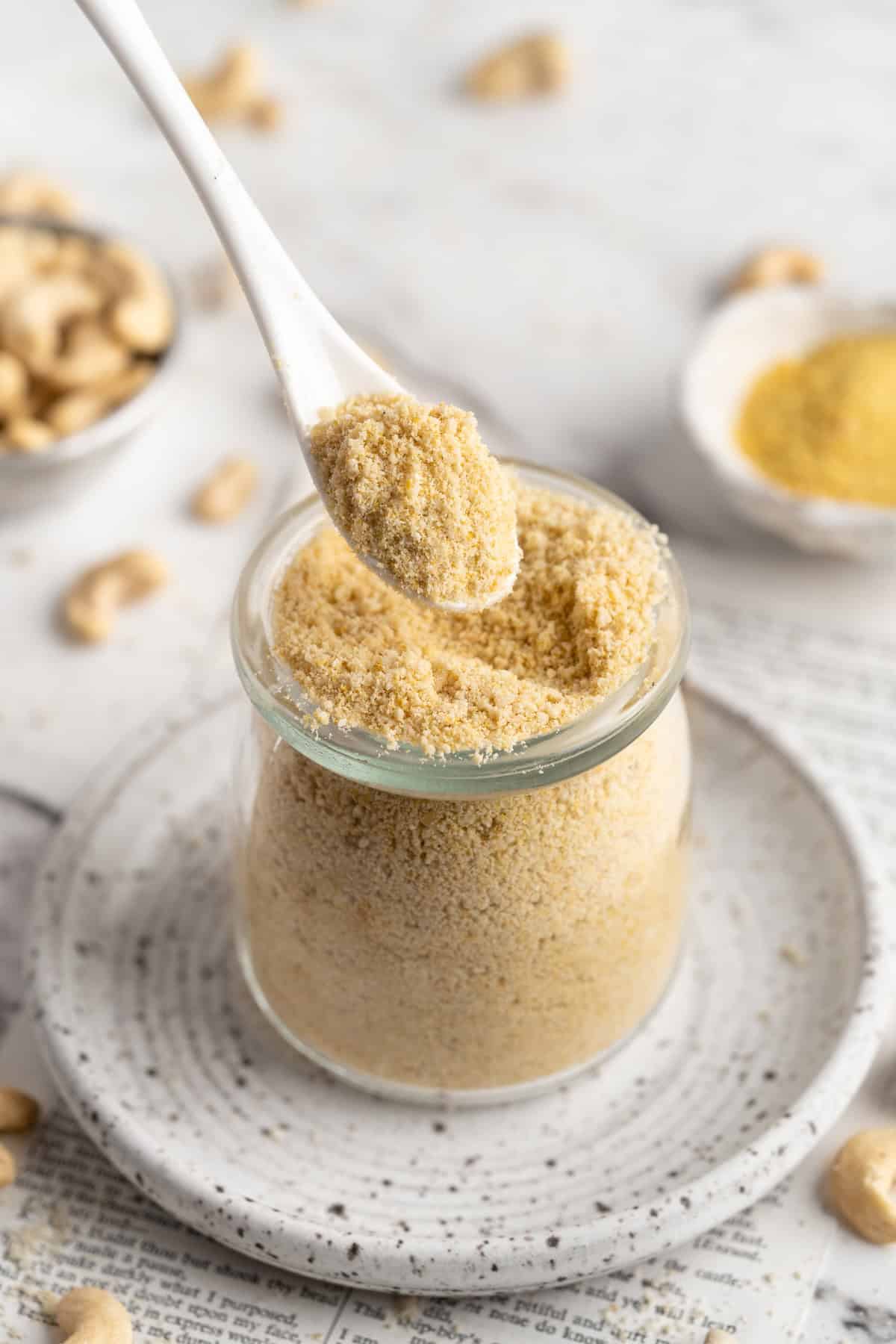 Spoonful of homemade vegan Parmesan cheese held over jar