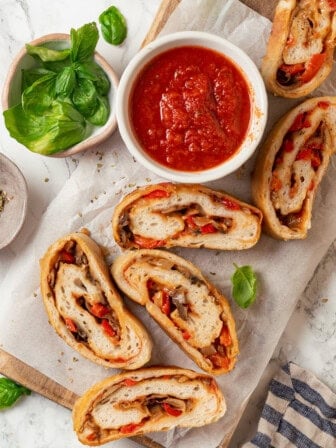 Overhead view of sliced stromboli on wooden board with bowl of marinara