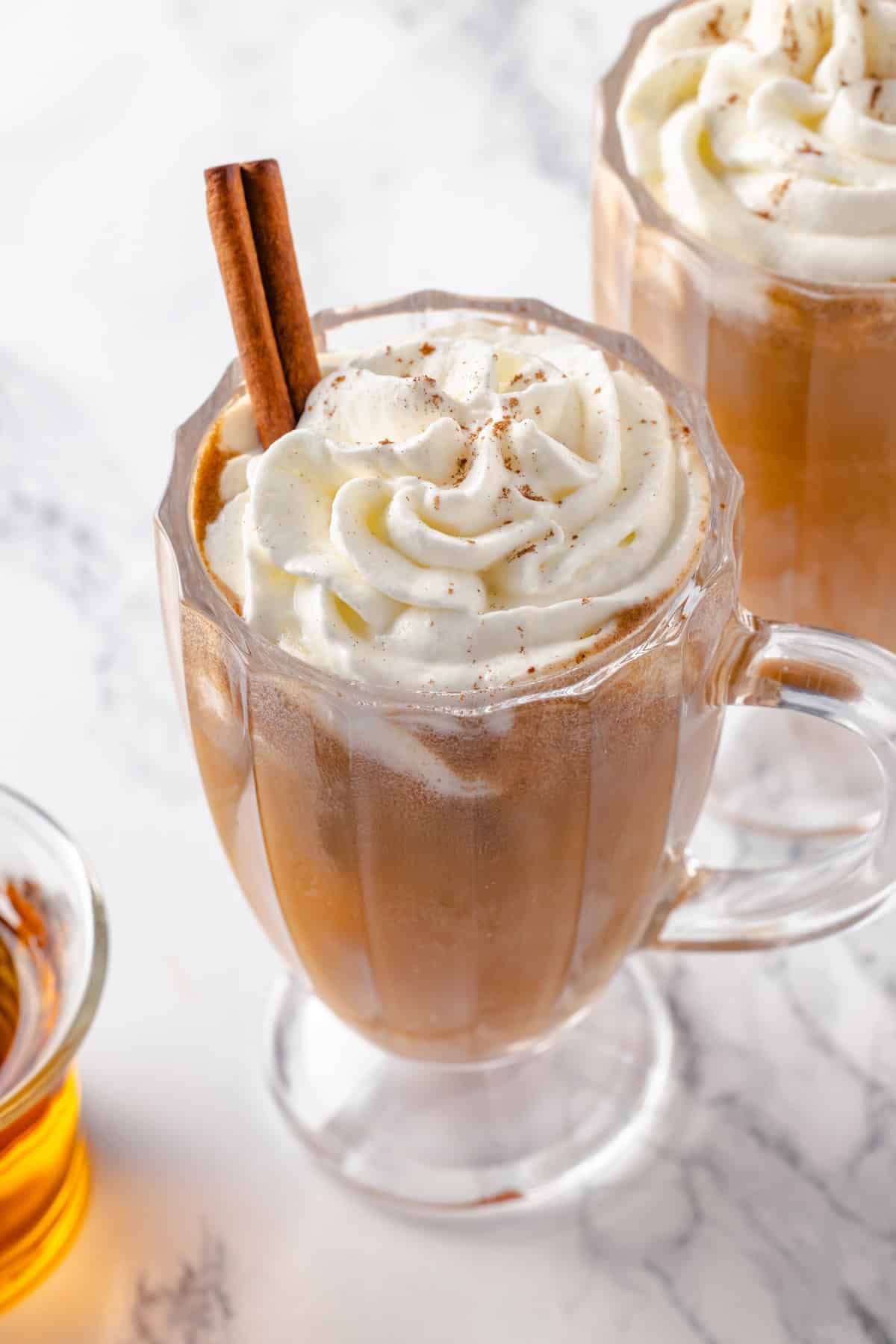 Glass mug of hot buttered rum with whipped cream and cinnamon stick