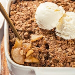 Spoon digging into vegan apple crisp in baking dish