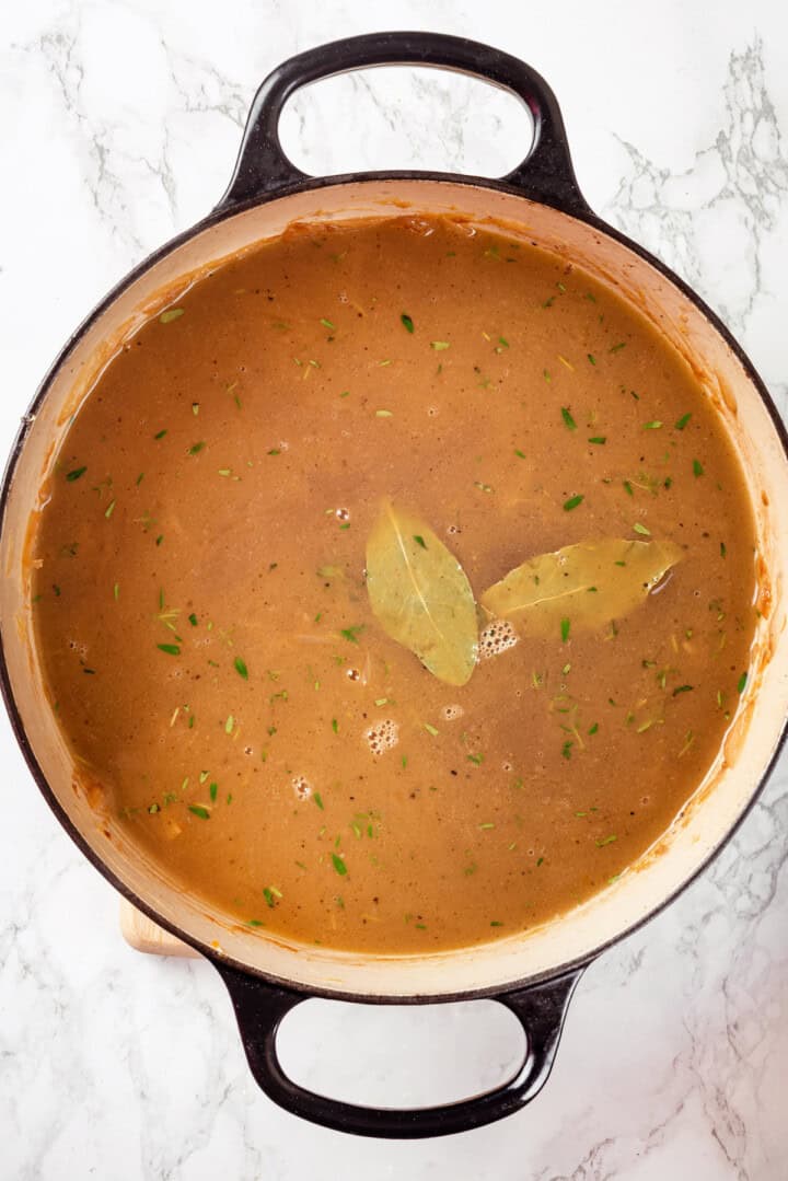 Overhead view of French onion soup in Dutch oven with bay leaves